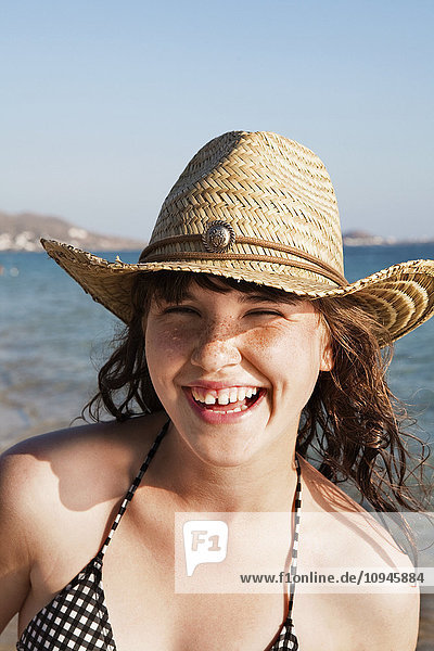 Portrait of smiling teenage girl wearing straw hat on beach