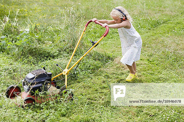 Mädchen mäht Garten mit Rasenmäher