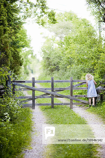 Mädchen steht vor einem Holztor auf einem Feldweg