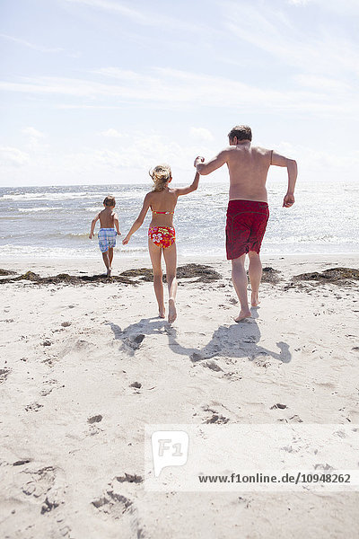 Vater mit Kindern läuft am Strand ins Meer