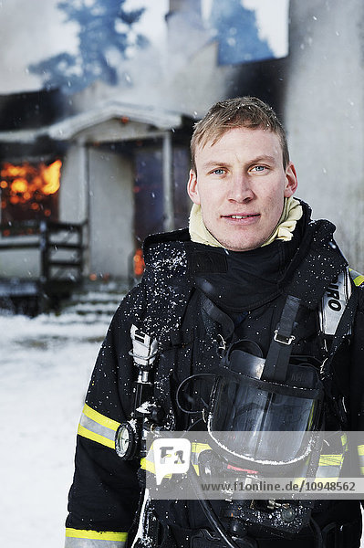 Portrait of firefighter in front of burning house