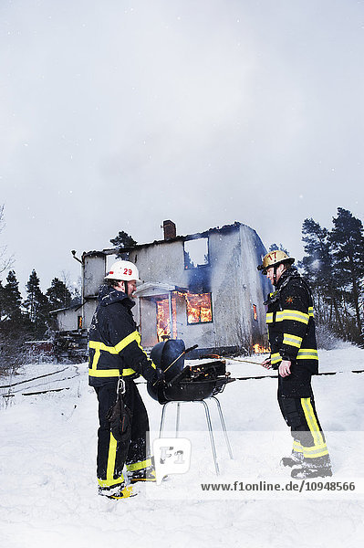 Feuerwehrleute beim Grillen vor einem brennenden Haus