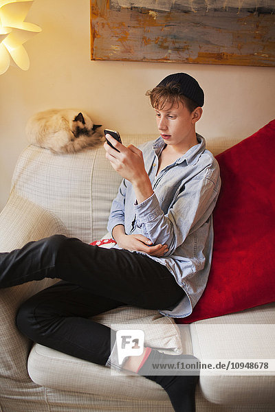 Teenage boy sitting on sofa and using cell phone