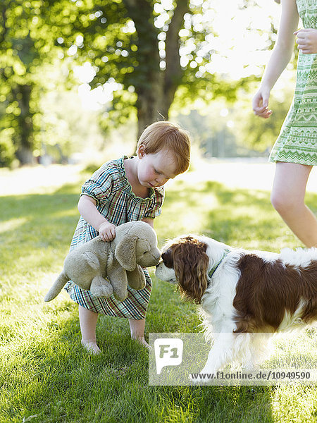Baby girl and older sister playing with dog in park