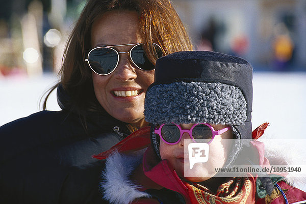 Porträt einer lächelnden Frau mit Sonnenbrille und einem Kind.