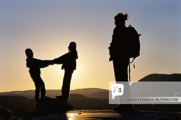 Family standing on mountain with sunset in the background.