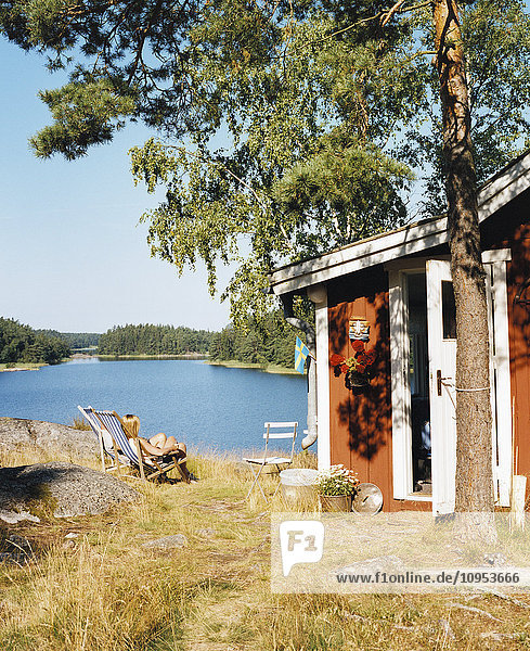 A woman sitting outside a red cottage by the sea  Sweden.