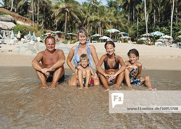Eine Familie sitzt am Strand in der Sonne am Wasser.