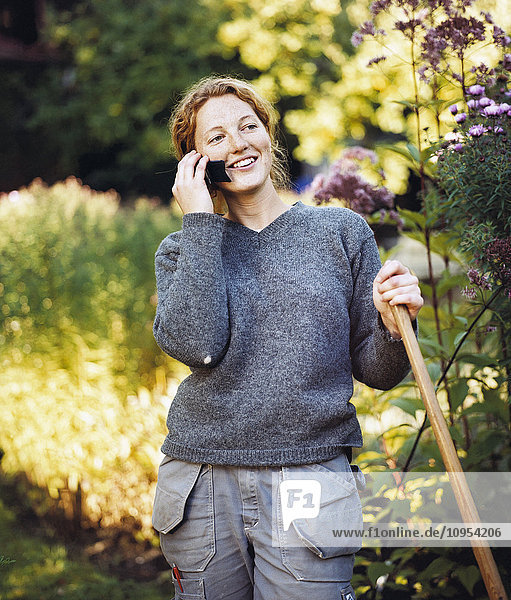Red-haired woman stands in the garden and talking on the phone.