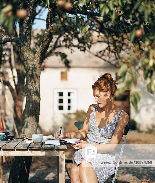 Frau im Garten schreibt in ein Notizbuch