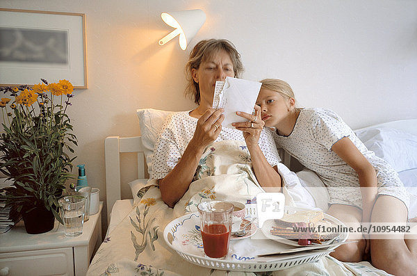 Mother and daughter lying in bed with breakfast tray and read the letter.
