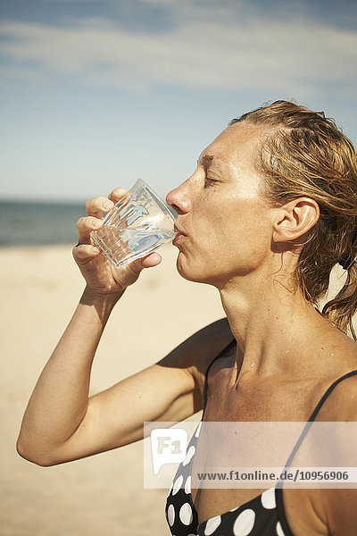 Frau trinkt ein Glas Wasser am Strand  Schweden.