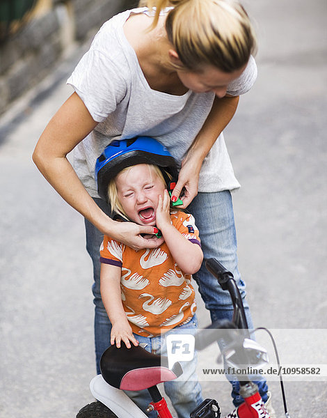 Mutter hilft einem weinenden Kind  einen Fahrradhelm aufzusetzen  Schweden.