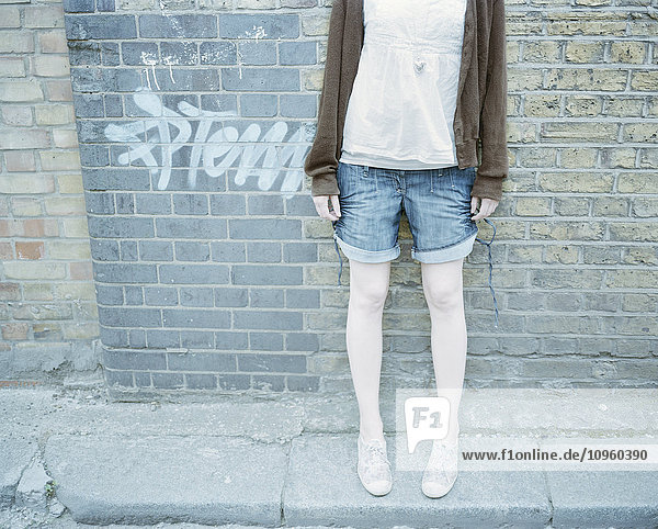 Young woman standing against brick wall  low section
