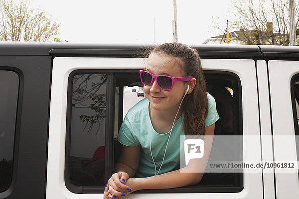 Mädchen im Vorschulalter mit Sonnenbrille und Kopfhörern  die aus dem Autofenster hängen; Asbestos  Quebec  Kanada
