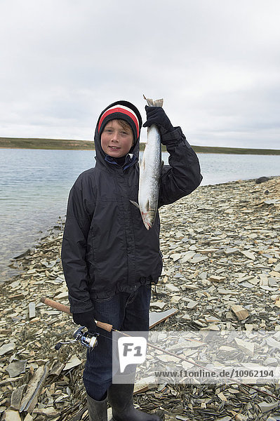 'Boy holds fresh caught Arctic Char while shore fishing in the Arctic Ocean  Western Arm  near Cambridge Bay; Nunavut  Canada'
