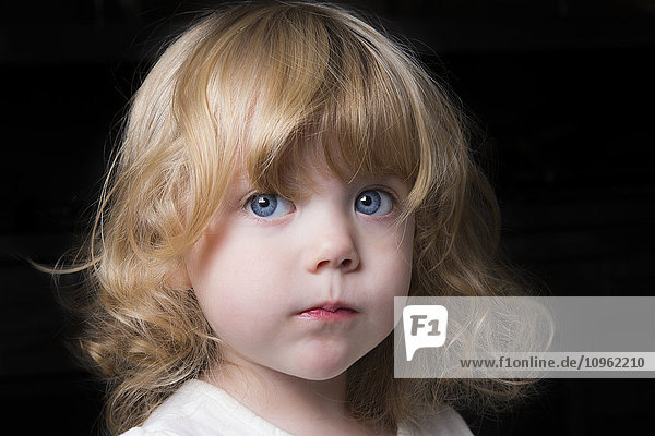 Porträt eines schönen jungen Mädchens mit großen blauen Augen und lockigem blondem Haar auf schwarzem Hintergrund; Spruce Grove  Alberta  Kanada'.