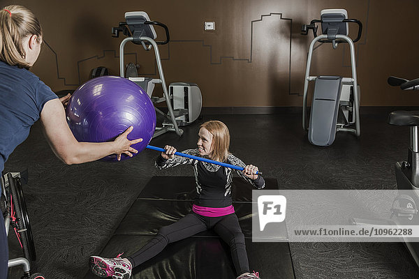 Physiotherapeutin  die einer jungen Frau mit einer Rückenmarksverletzung bei der Durchführung von Übungen zum Werfen eines Widerstandsballs hilft; Edmonton  Alberta  Kanada .