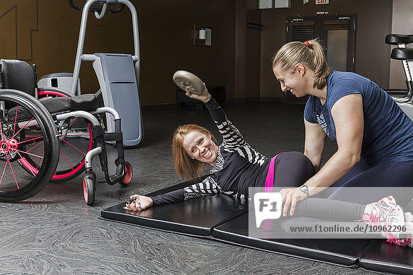 Physiotherapeutin  die einer jungen Frau mit einer Rückenmarksverletzung bei der Ausführung von Oberkörper-Windschutzscheibenwischern und gewichteten schrägen Drehungen hilft; Edmonton  Alberta  Kanada .