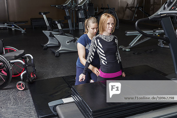 Physiotherapeutin  die einer jungen Frau mit einer Rückenmarksverletzung bei der Durchführung von Gleichgewichtsübungen mit hohen Knien und ohne Hände hilft; Edmonton  Alberta  Kanada
