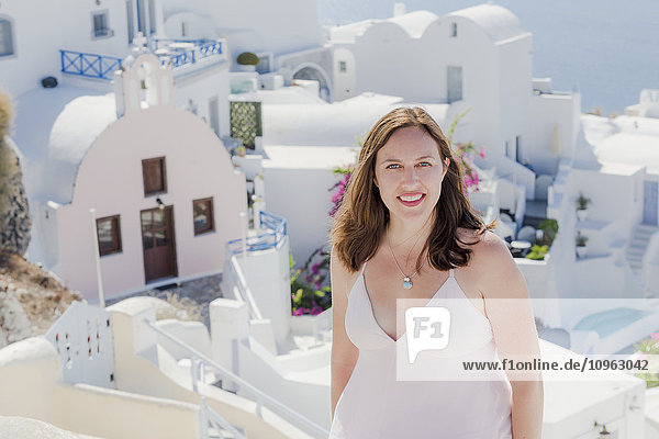 Eine Frau posiert vor einer weiß getünchten Kirche und Gebäuden im Hintergrund; Santorin  Griechenland'.