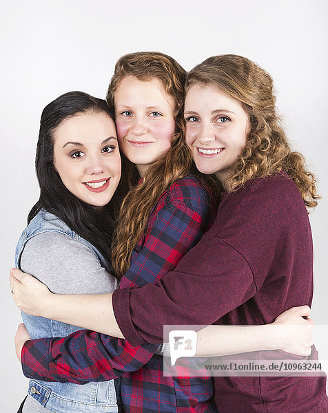 'Portrait of three young women hugging each other  on a white background; Alberta  Canada'