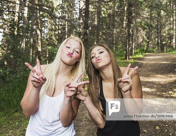 'Two girlfriends doing a selfie expression on a pathway in a park; Edmonton  Alberta  Canada'