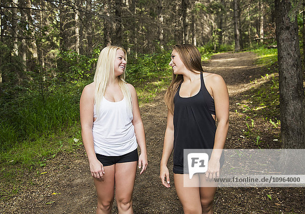 Zwei Freundinnen im Teenageralter  die gemeinsam auf einem Weg in einem bewaldeten Park spazieren gehen und sich unterhalten; Edmonton  Alberta  Kanada