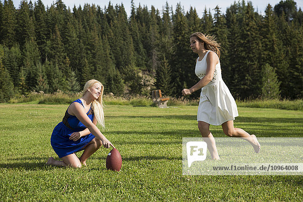 'Two girlfriends playing football in a park in their dresses; Edmonton  Alberta  Canada'