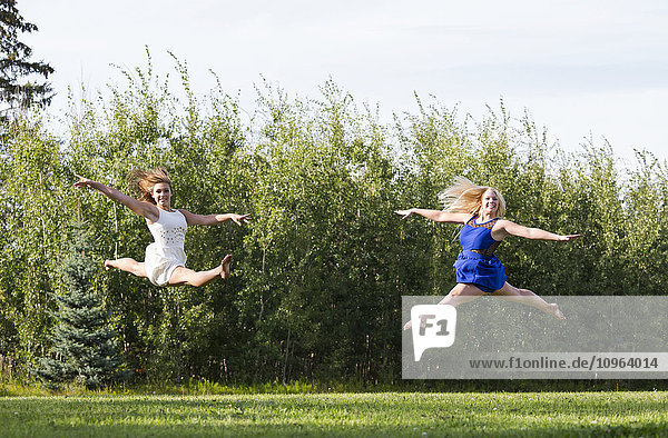 'Two gymnast girlfriends practicing their split jumps in a park in their dresses; Edmonton  Alberta  Canada'