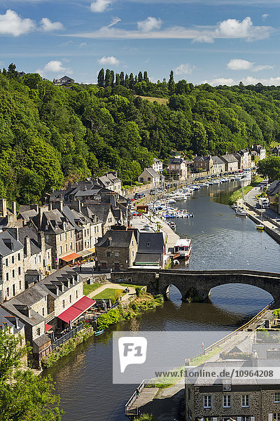 Stadt am Fluss mit bewaldetem Tal  Steinbrücke und Booten im Hafen mit blauem Himmel und Wolken; Dinan  Bretagne  Frankreich'.