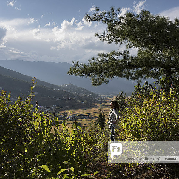 'A woman stands looking out over Paro Valley; Paro  Bhutan'