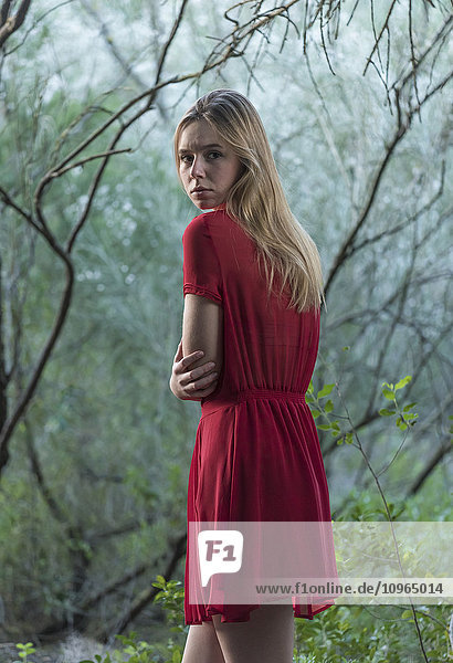 'A girl wearing a red dress with blond hair looking unsure as she walks among trees; Tarifa  Cadiz  Andalusia  Spain'