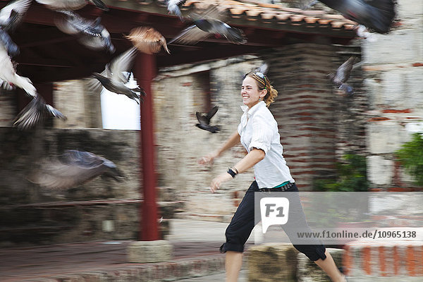 'A young woman runs after a flock of birds taking flight; Cartagena  Columbia'