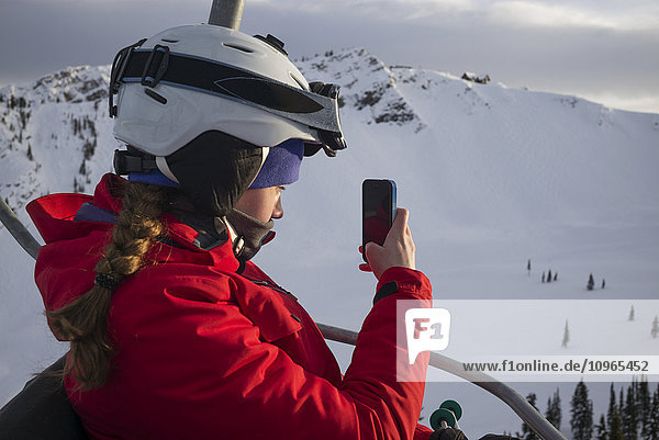 'A skier on a chair lift at a ski resort takes a picture with a smart phone  Banff national park; Alberta  CanadaNone'