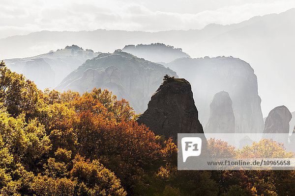 'Low cloud around the rugged cliffs with foliage in autumn colours; Meteora  Greece'