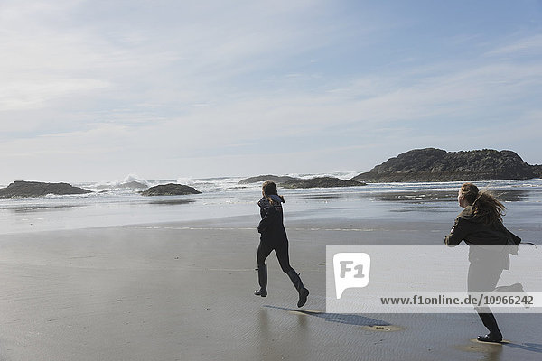 'Teenage girls running on a wet beach at the coast  Vancouver Island; Tofino  British Columbia  Canada'
