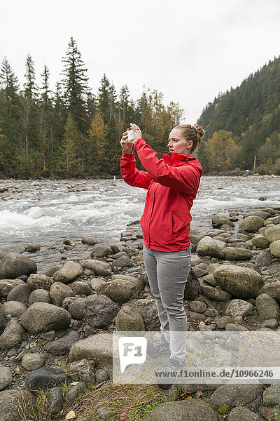 Eine Frau steht am felsigen Ufer des Chilliwack River und fotografiert; Chilliwack  British Columbia  Kanada .