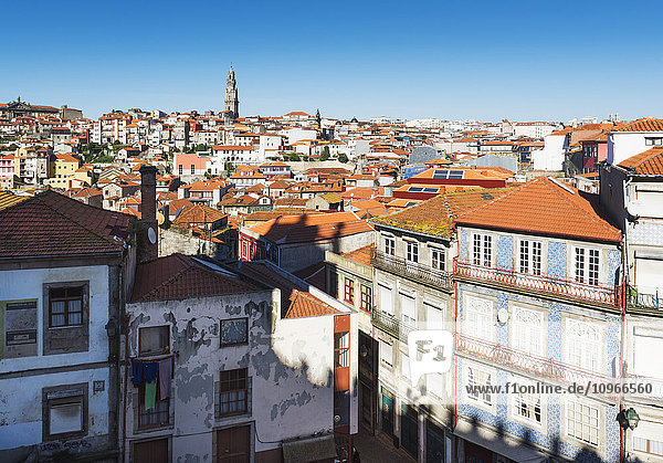 'Rooftops of houses and a tower in the distance against a blue sky; Oporto  Portugal'