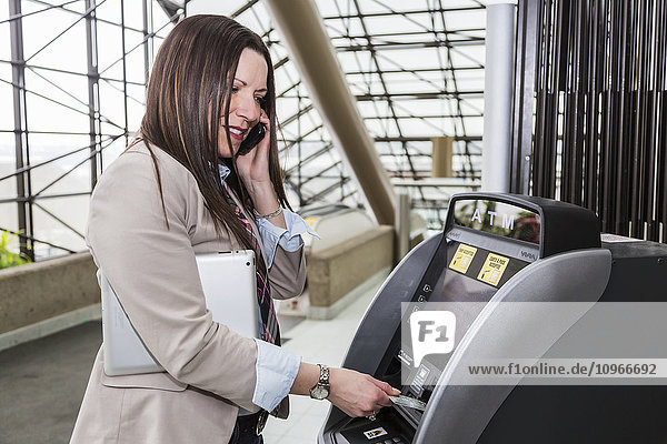 'Mature business woman making a cash withdrawal at an ATM in the atrium of an office building; Edmonton  Alberta  Canada'