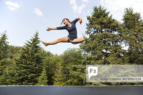'Teenage girl jumping high in the air outdoors on a trampoline; Sherwood Park  Alberta  Canada'
