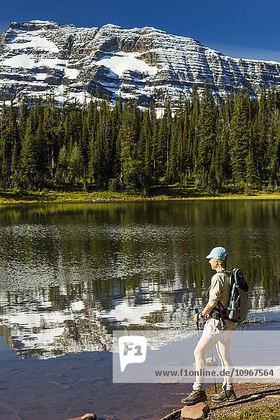 Wanderin steht am Ufer eines Bergsees  in dem sich Schneegipfel und blauer Himmel spiegeln; Waterton  Alberta  Kanada'.
