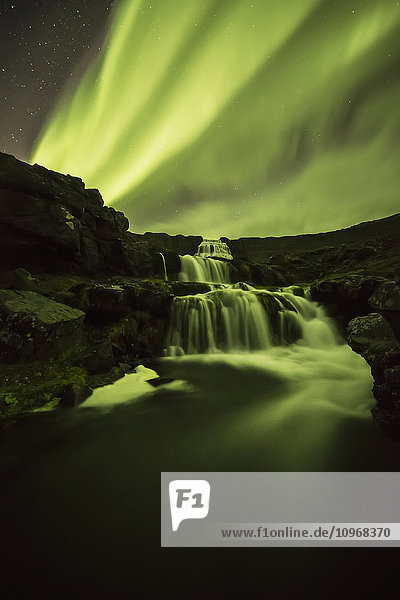 'Northern Lights or Aurora Borealis glowing over waterfalls and a stream; Iceland'
