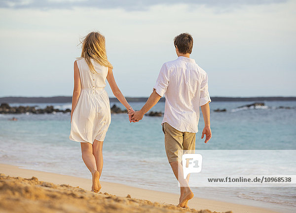 Romantic happy couple walking on beach at sunset. Smiling holding hands. Man and woman in love