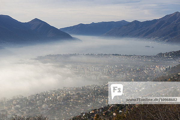 'Fog sets in over a city and alpine lake; Locarno  Ticino  Switzerland'