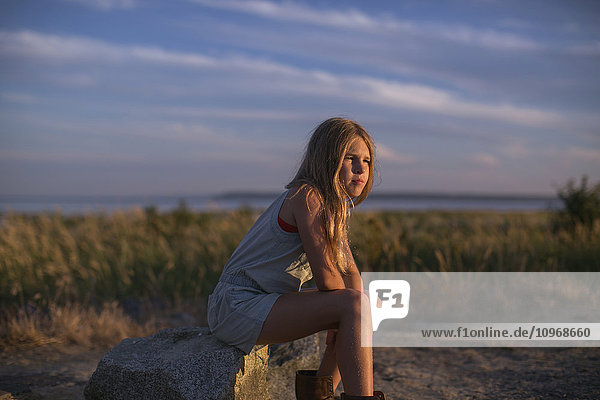 'Girl in contemplation sitting on a rock on the beach at sunset; Surrey  British Columbia  Canada'