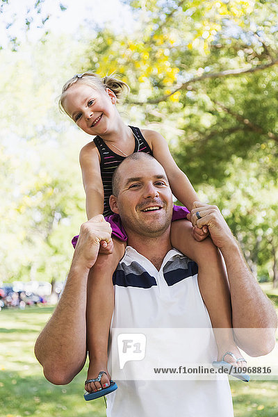 'Father carrying his daughter on his shoulders in a park in autumn; Edmonton  Alberta  Canada'
