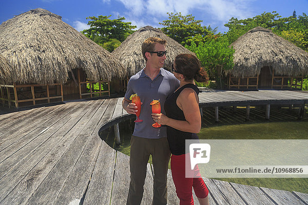 Paar auf einer Holzpromenade mit erfrischenden Getränken im Saint Georges Caye Resort; Belize City  Belize'.