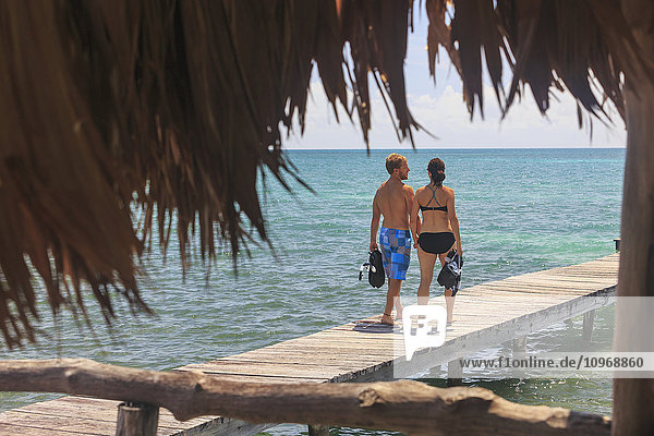 Ein Paar geht auf einem Holzsteg mit Schnorchelausrüstung spazieren  Saint Georges Caye Resort; Belize City  Belize'.