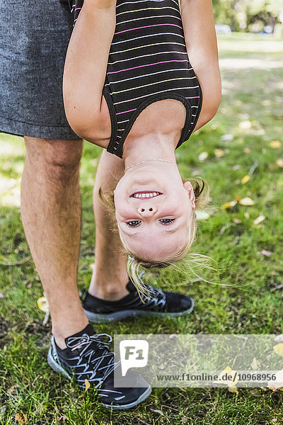 'A father hanging his daughter upside down and playing around in a park during a family outing; Edmonton  Alberta  Canada'